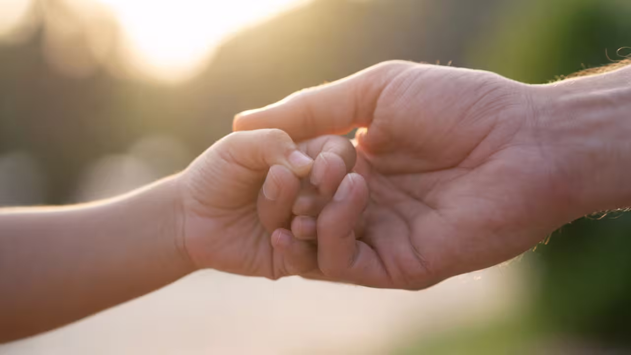Close-up of an adult gently holding a child’s hand for comfort and support.