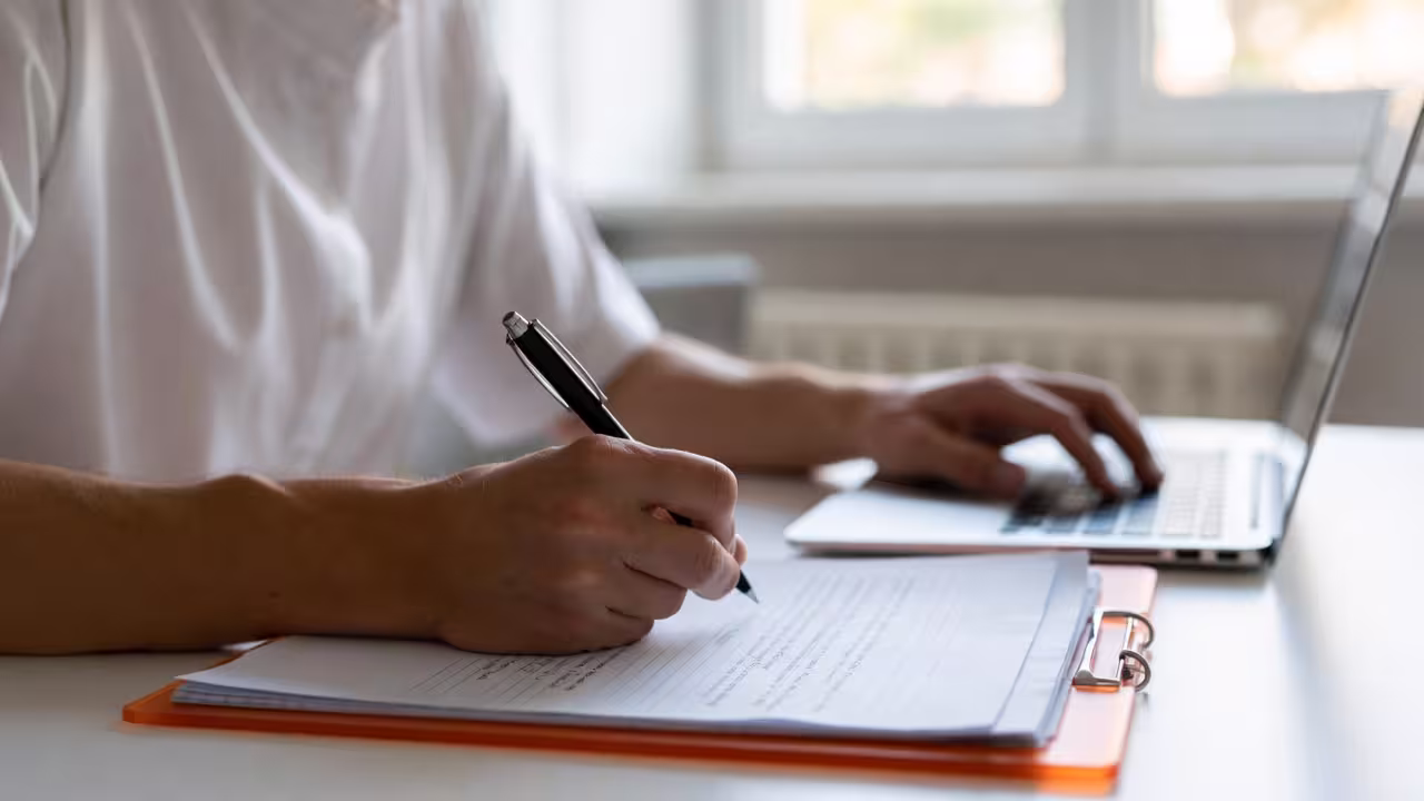Caregiver writing notes at a desk while organizing family support tasks.