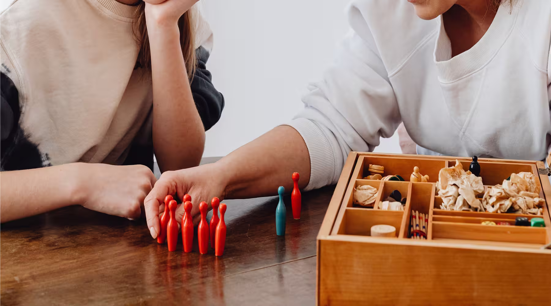 Adult and child arranging colored counting figures beside a wooden activity tray.