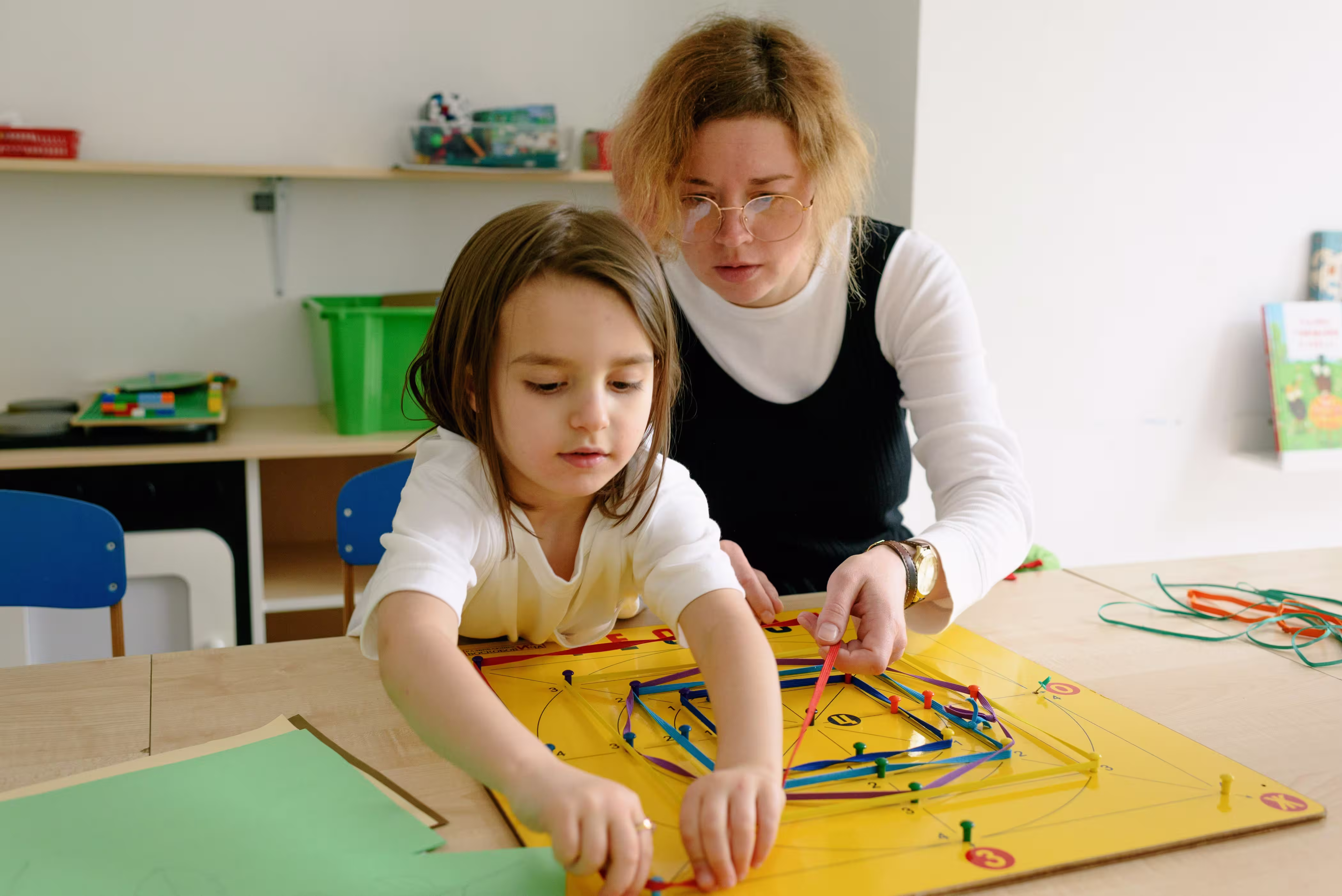 Adult supporting a child using a numbered pegboard and colored bands.