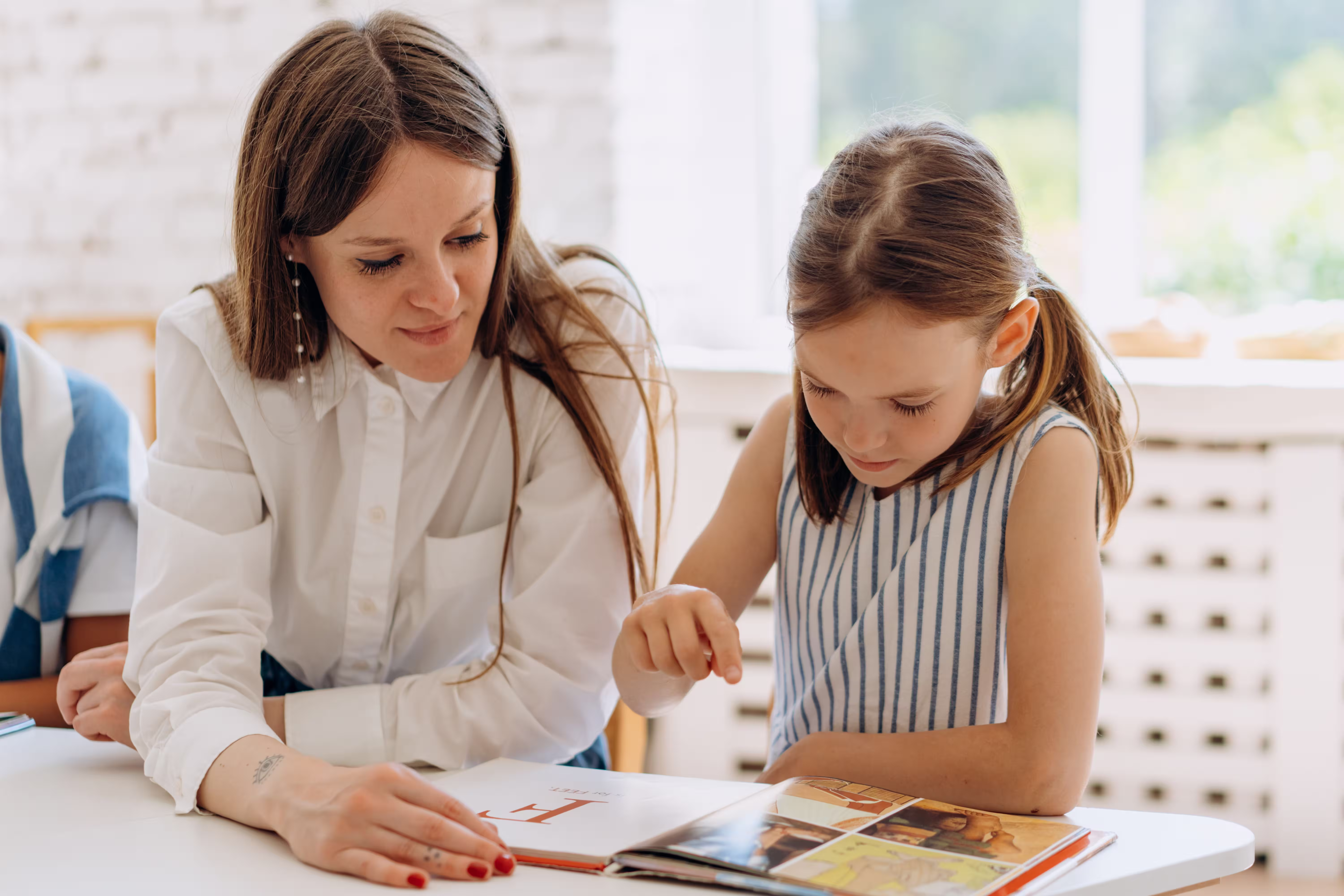 Adult sitting beside a child as they follow along in an open book.