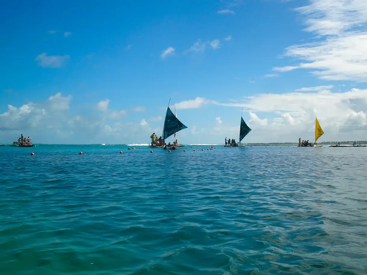Three traditional sailboats with blue and yellow sails on calm ocean water under a partly cloudy sky.