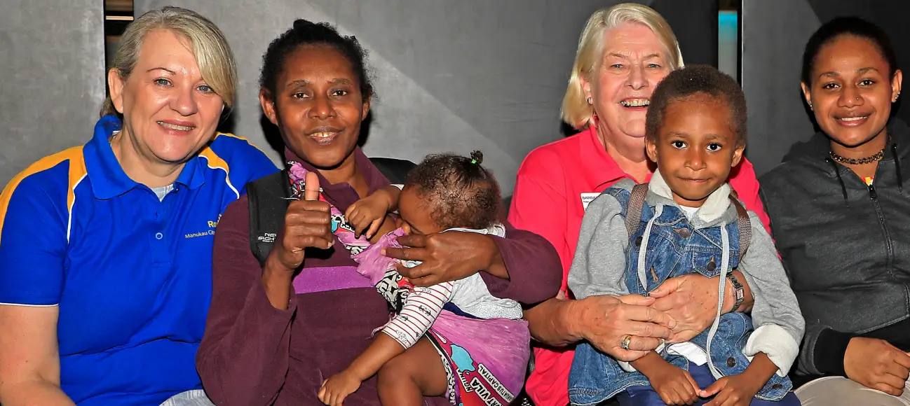 Group of six people, including two children, smiling and sitting together indoors against a plain background.