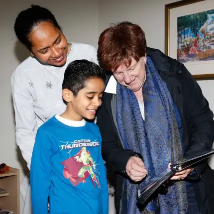 A woman and a child smiling while looking at a clipboard held by an elderly woman wearing a blue scarf.