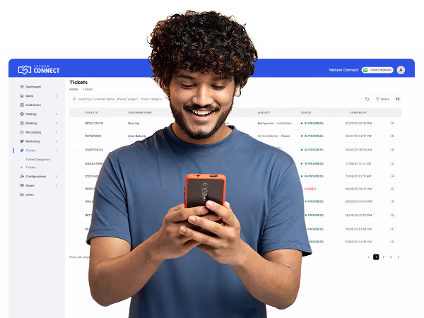 Smiling young man with curly hair using a smartphone with a ticket management software interface in the background.