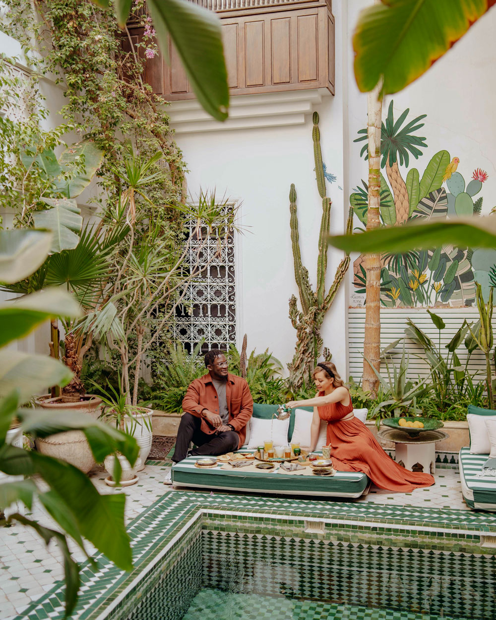Travel creator Cindy sharing tea with her husband poolside inside a beautifully tiled riad in Marrakech
