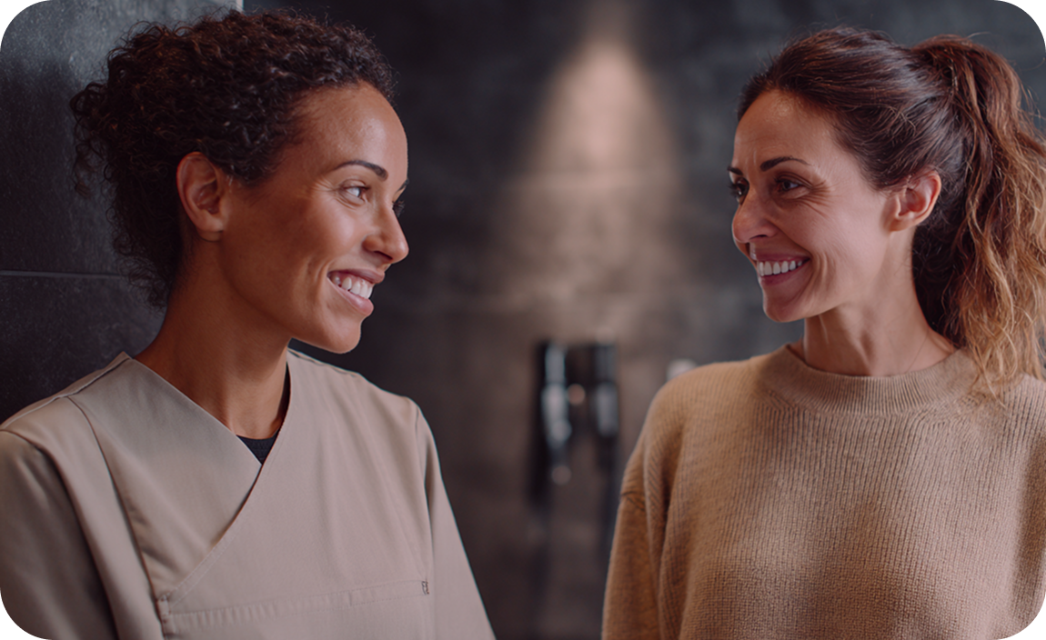Two women standing and speaking together in a clinical setting during a follow-up discussion