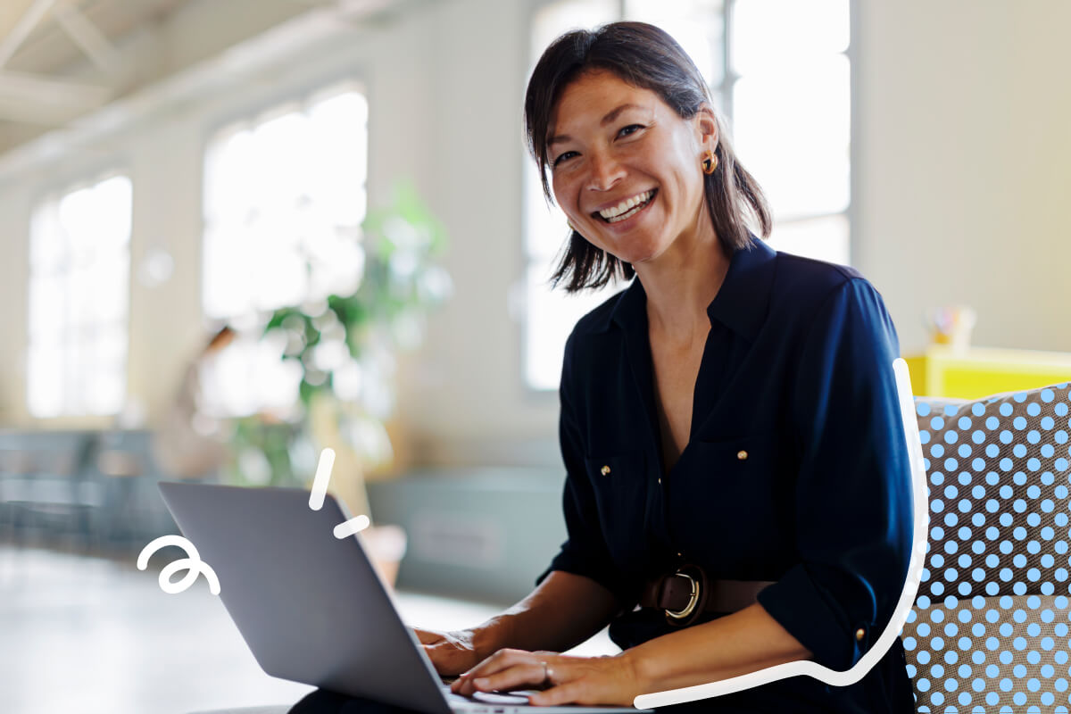 Donna sorridente con camicia blu scura che usa un laptop in un ufficio luminoso e moderno.