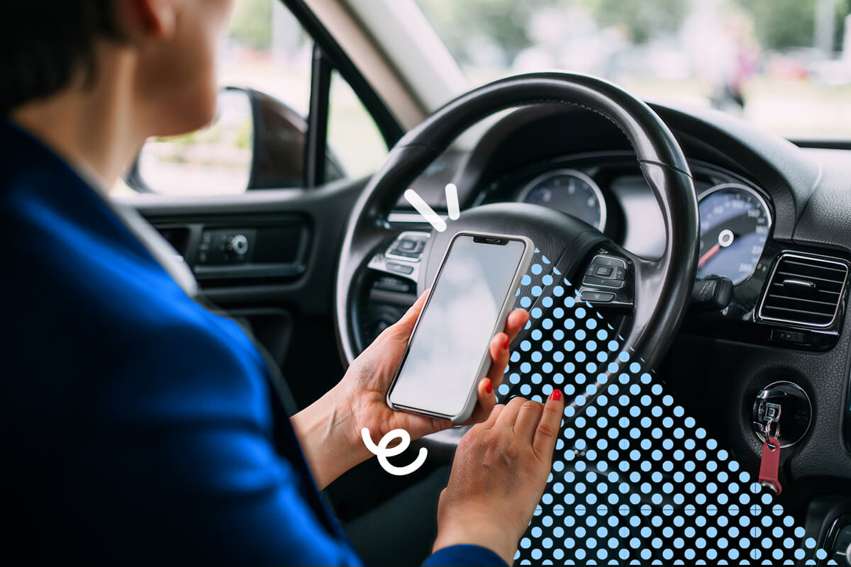 Persona seduta in auto che utilizza un telefono cellulare con schermo vuoto davanti al volante.
