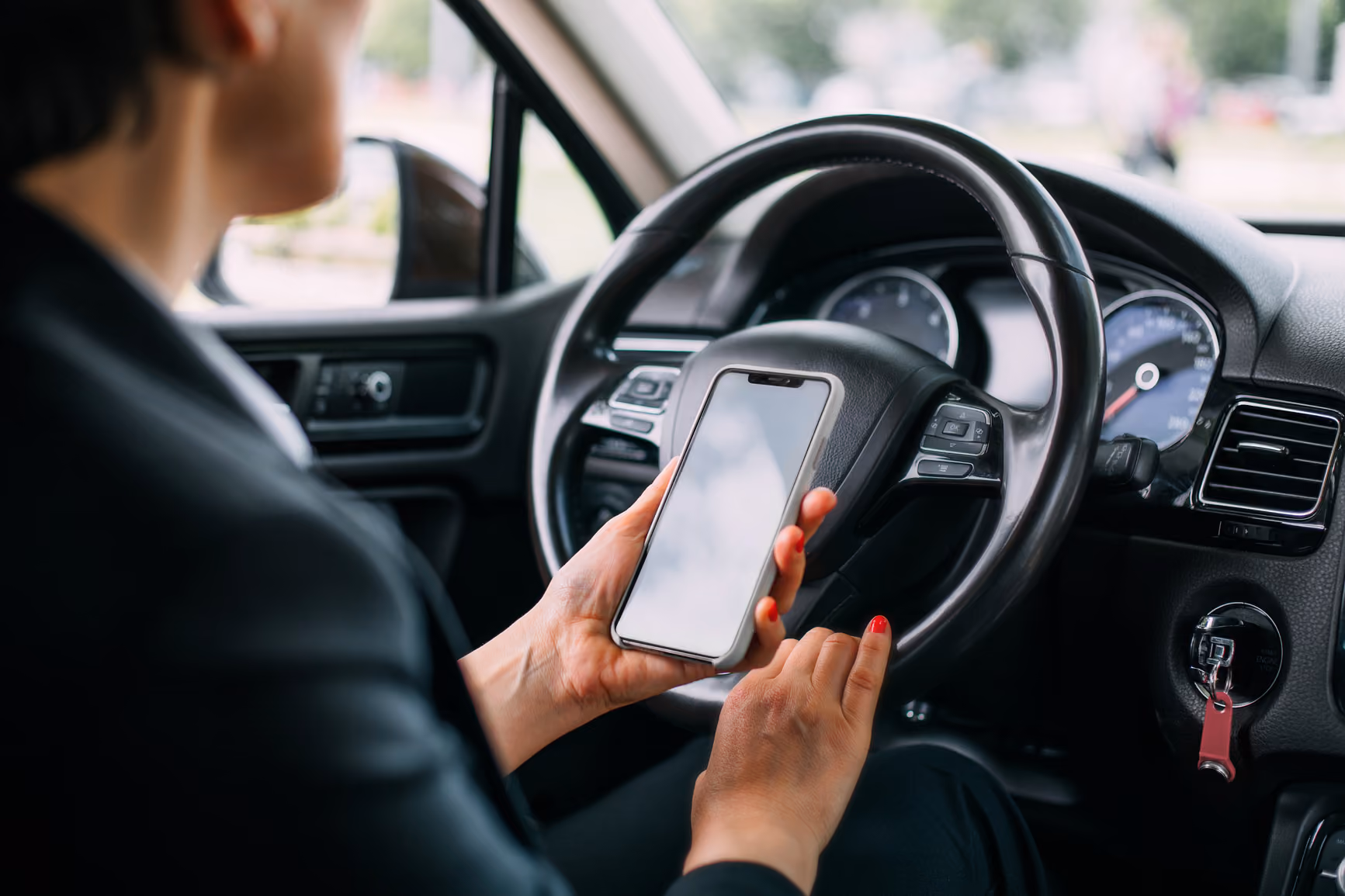 Persona seduta al volante di un'auto, che tiene uno smartphone con schermo vuoto nella mano destra.