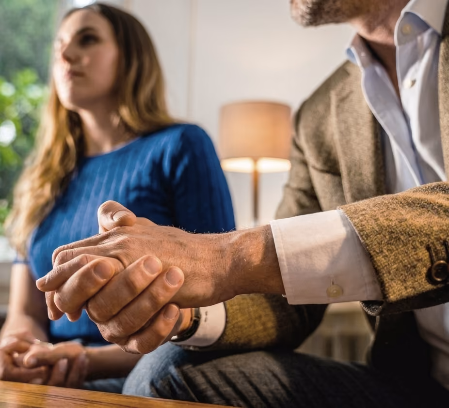 Due persone sedute insieme, una stringe le mani visibilmente preoccupata, l'altra è sfocata.