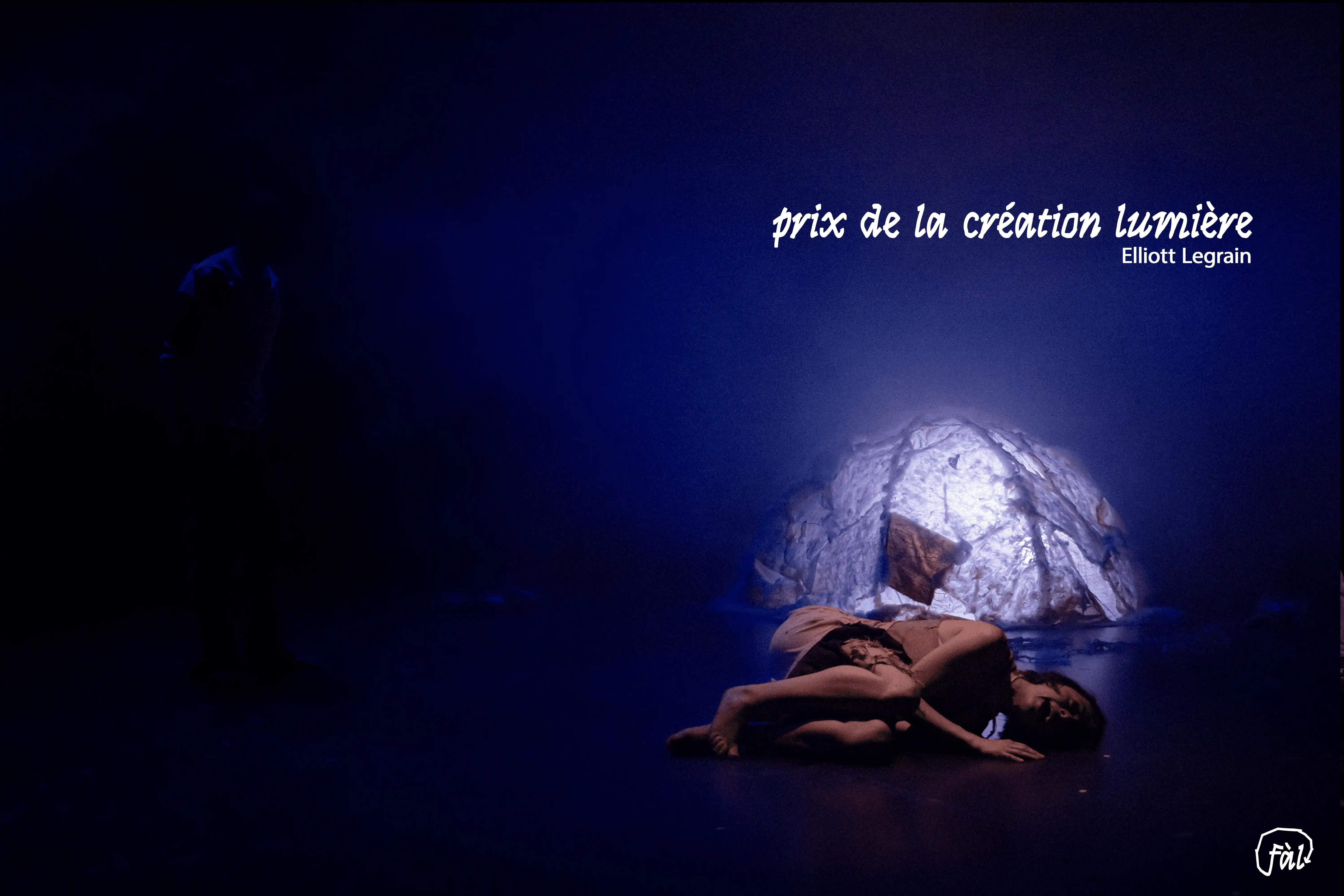 Scène baignée d’une lumière bleutée, performeuse allongée au sol devant un décor lumineux — texte “prix de la création lumière – Elliott Legrain”.