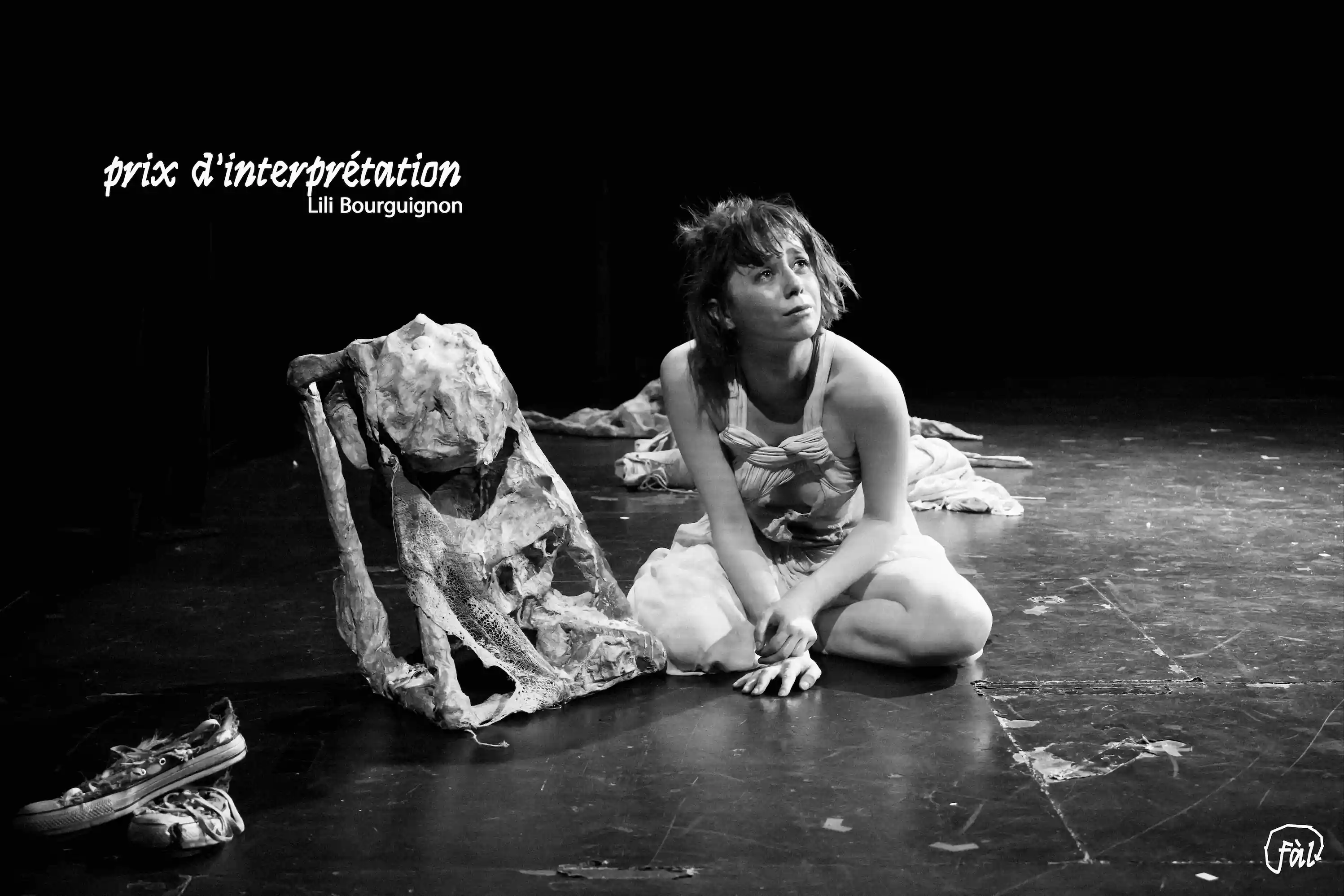 Performeuse à genoux sur scène, interagissant avec une sculpture organique en tissu et pierre, ambiance théâtrale en noir et blanc.