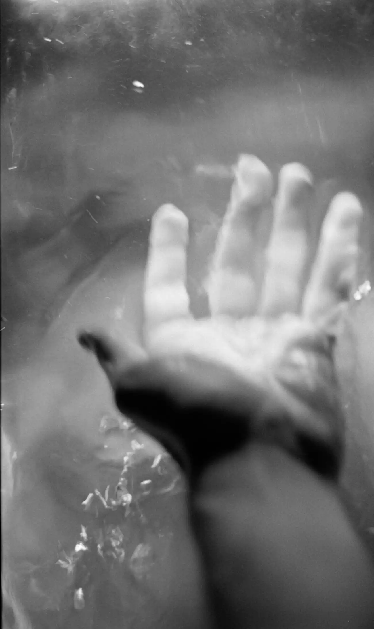 Photographie en noir et blanc d’une main tendue vers une surface translucide, évoquant la communication et le contact.