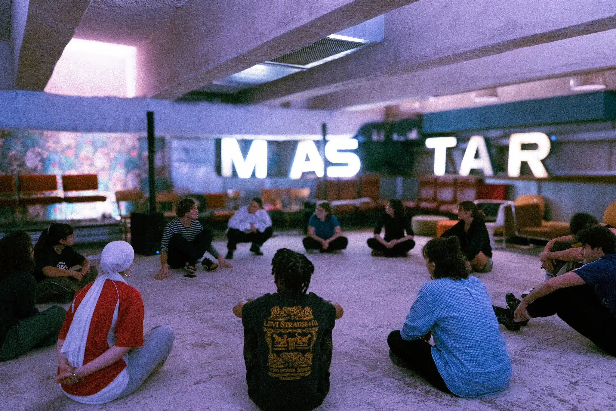 Groupe de personnes assises en grand cercle dans un atelier lumineux, entourées d’objets décoratifs.