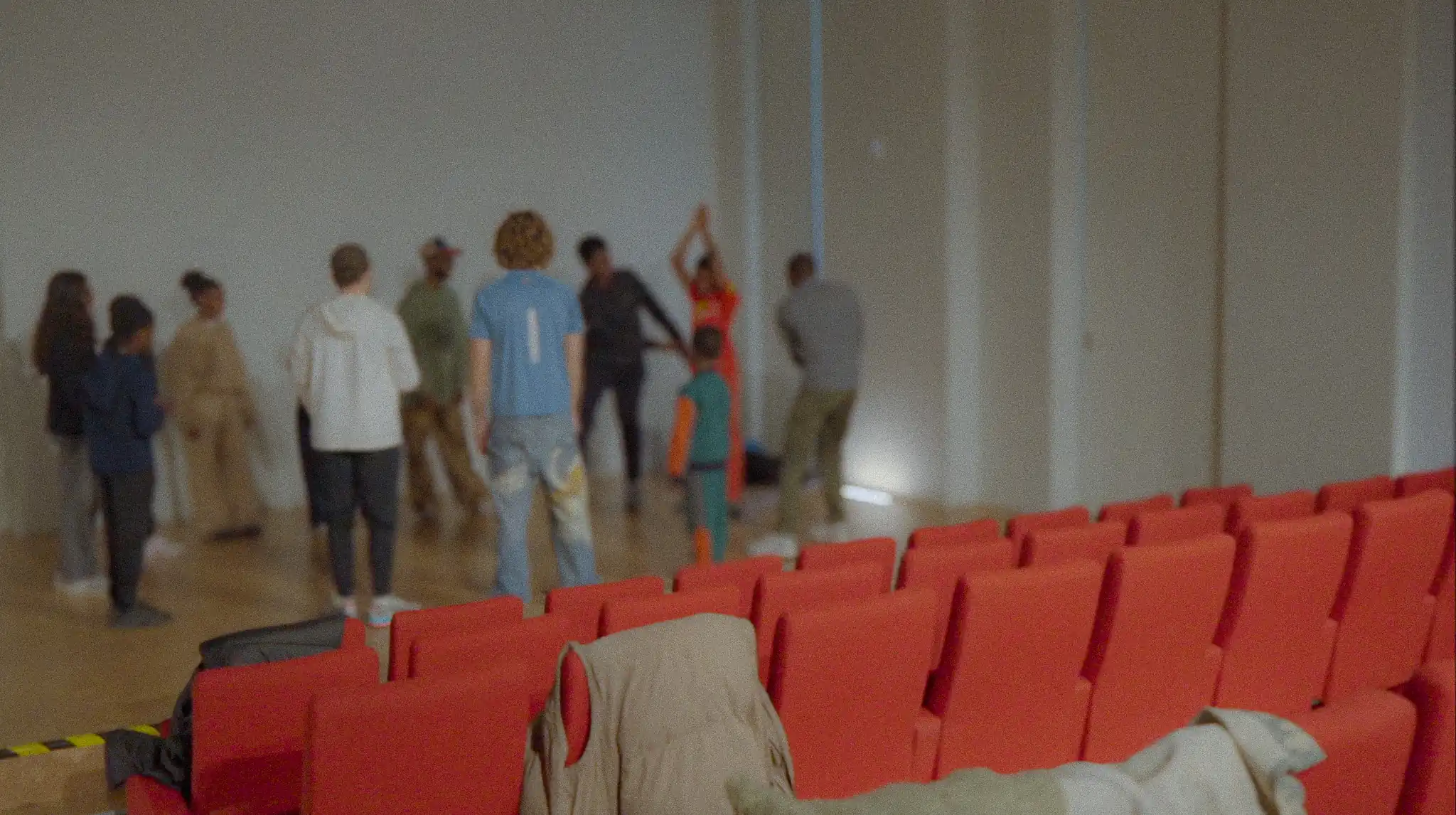Répétition collective dans une salle de spectacle, avec plusieurs participants debout sur scène et des sièges rouges au premier plan.