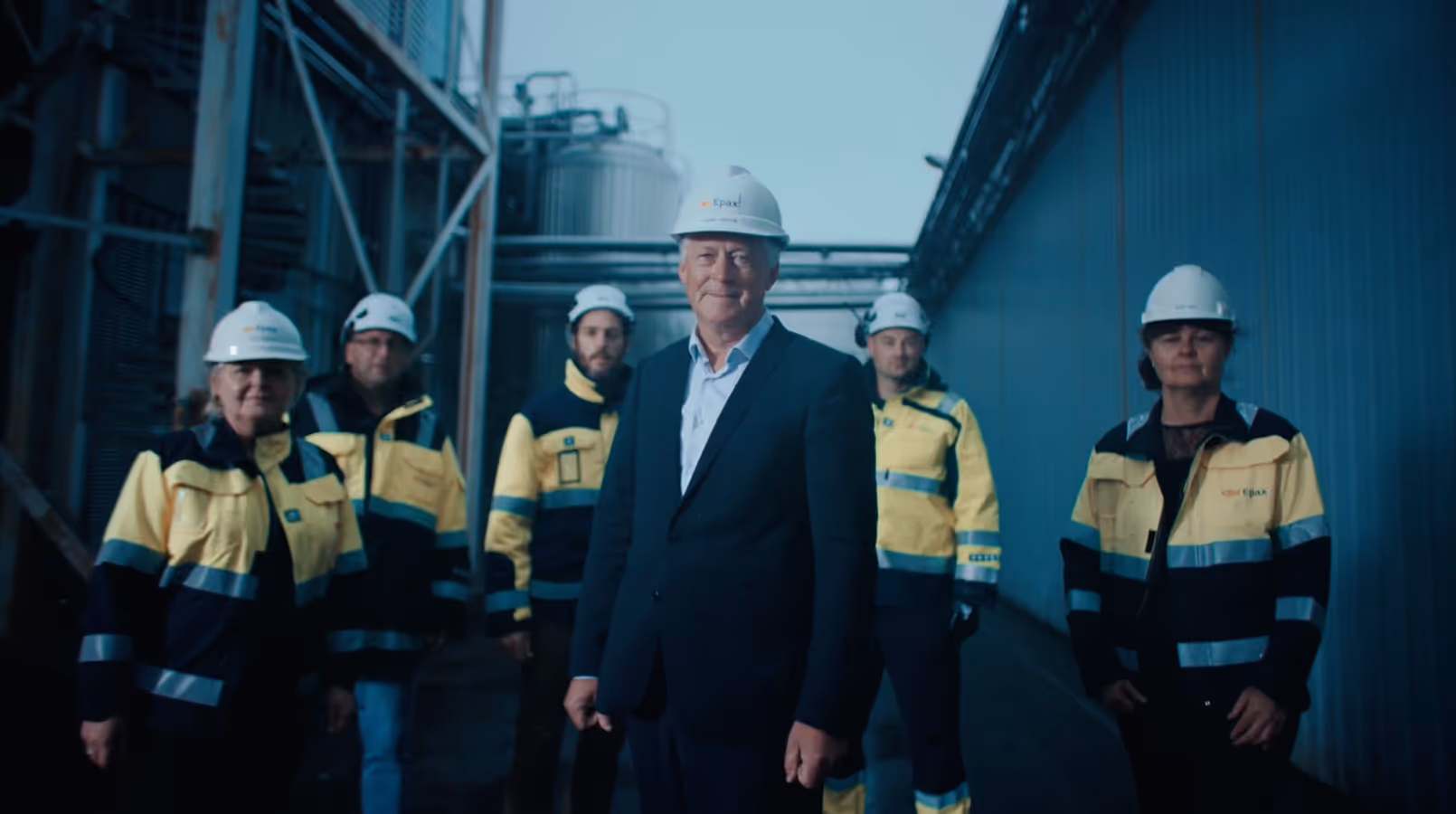 Group of six Epax workers wearing yellow and black safety jackets and white hard hats standing outdoors at the Epaxl facility.