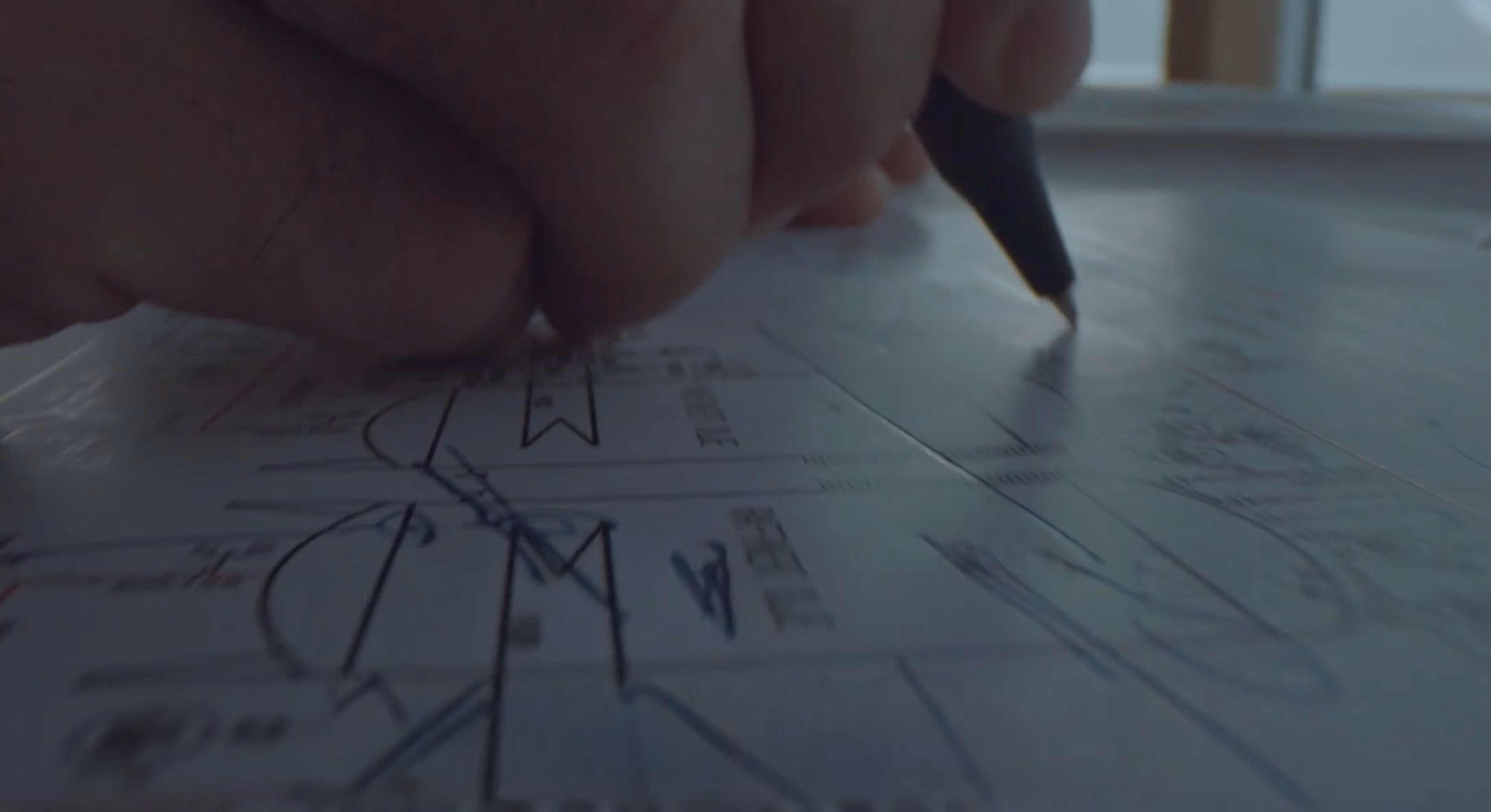 Close-up of a hand holding a black pen and making notes on a technical drawing or blueprint.