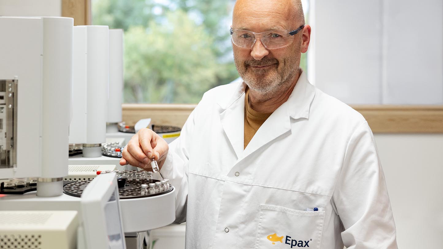 Smiling Epax scientist in white lab coat and safety glasses working with vials filled with Omega-3 fish oil in a laboratory.