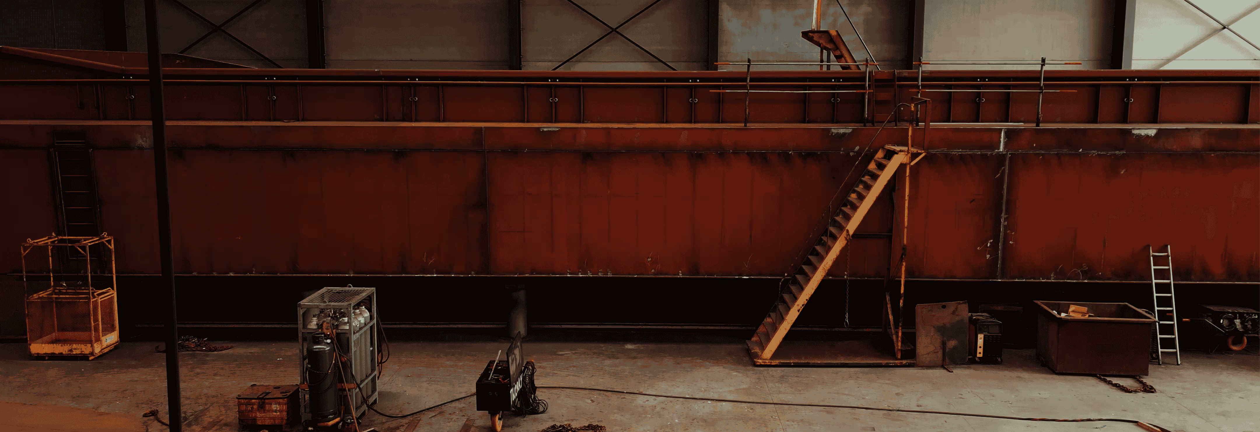 Industrieel magazijn met rode metalen wand, ladder en gereedschap.