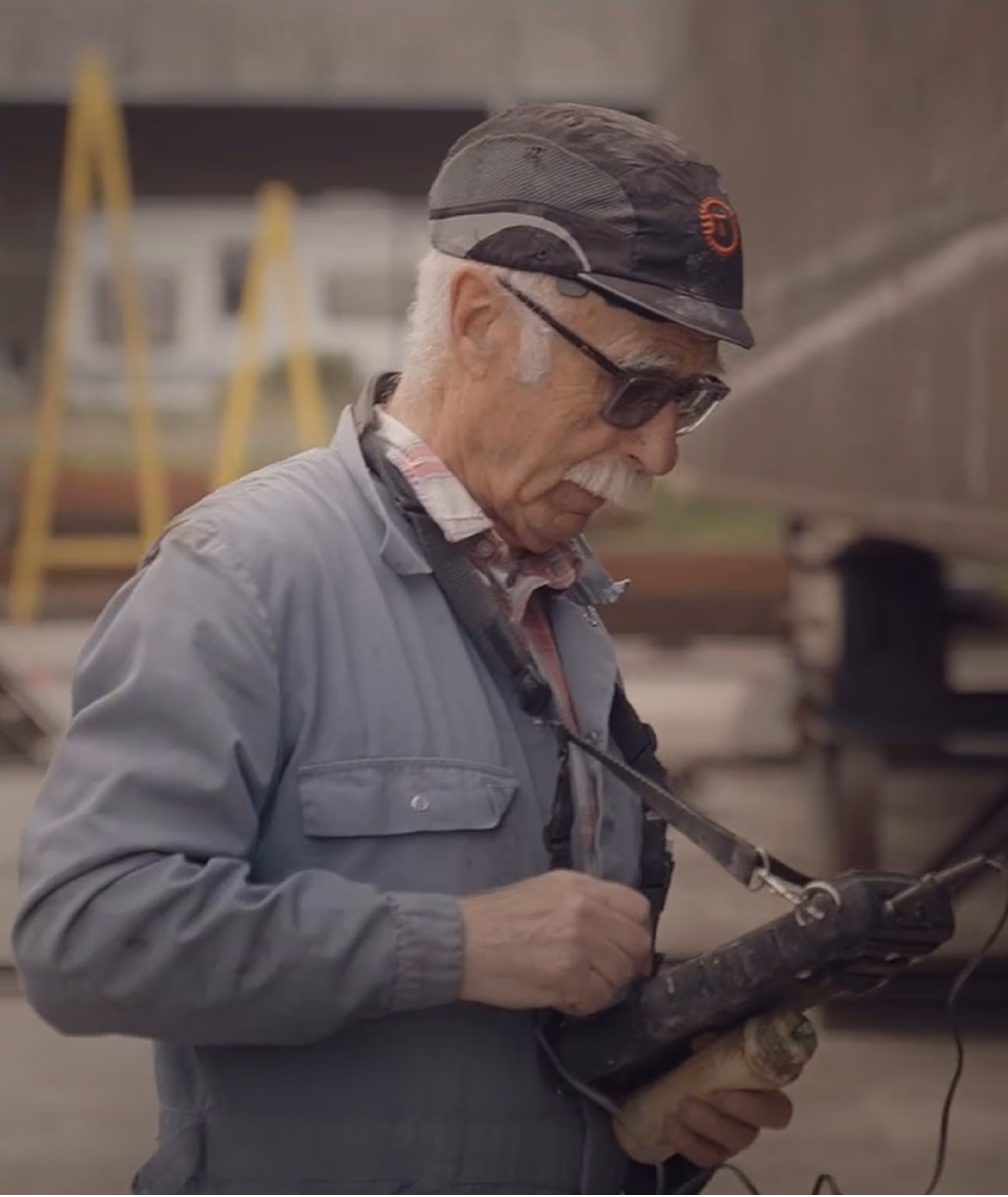 Oude man in werkkleding met lasapparaat buiten.
