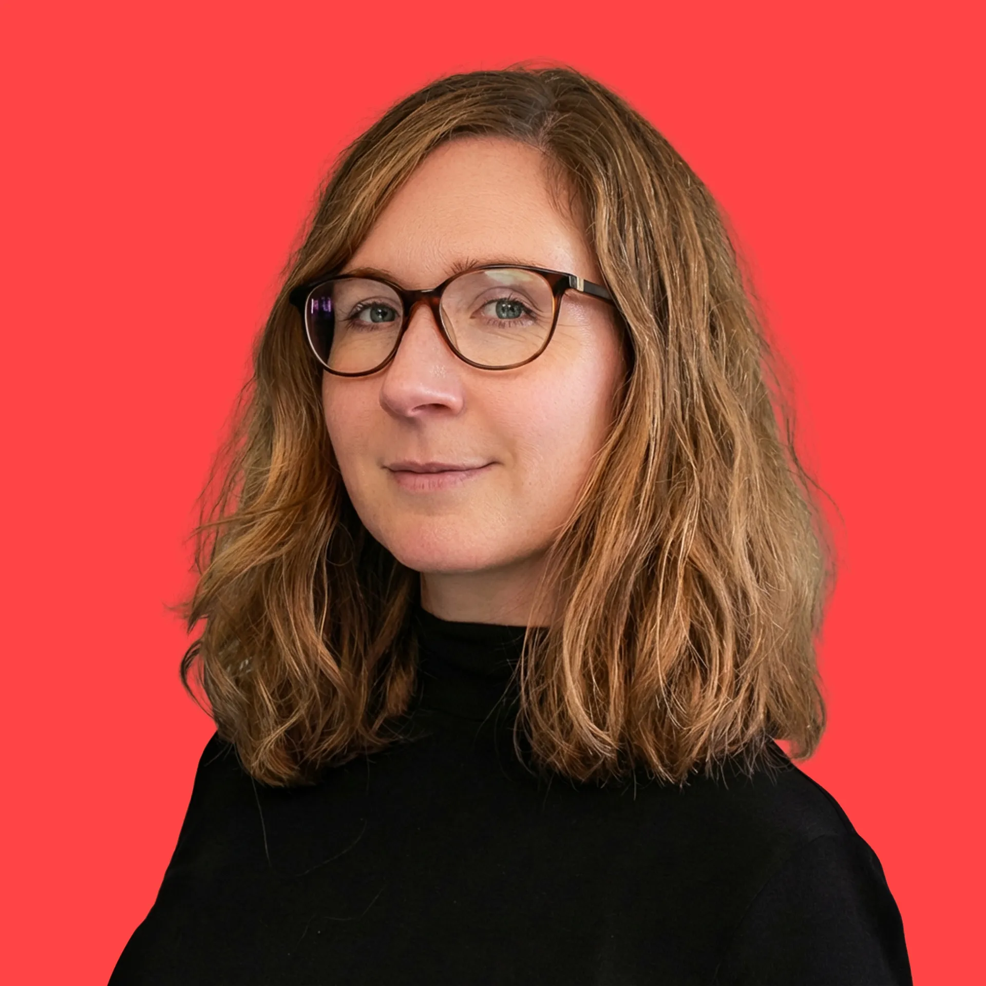 Frau mit schulterlangen, braunen Haaren und Brille vor rotem Hintergrund, trägt schwarzen Pullover.