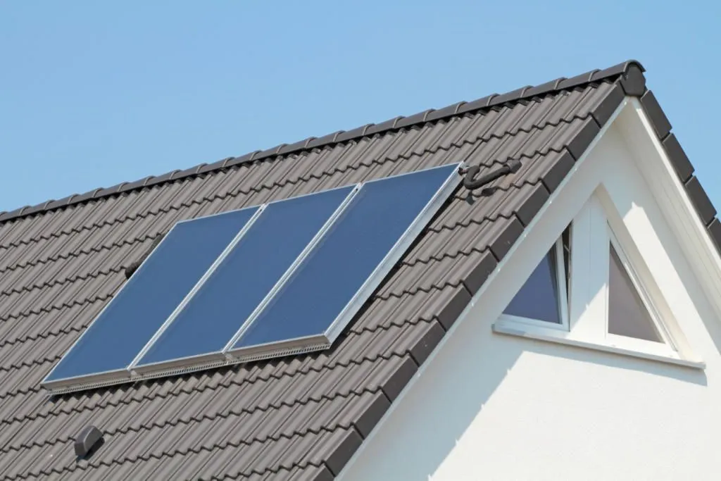 Dach eines Hauses mit drei Solarthermie-Paneelen unter klarem blauem Himmel.