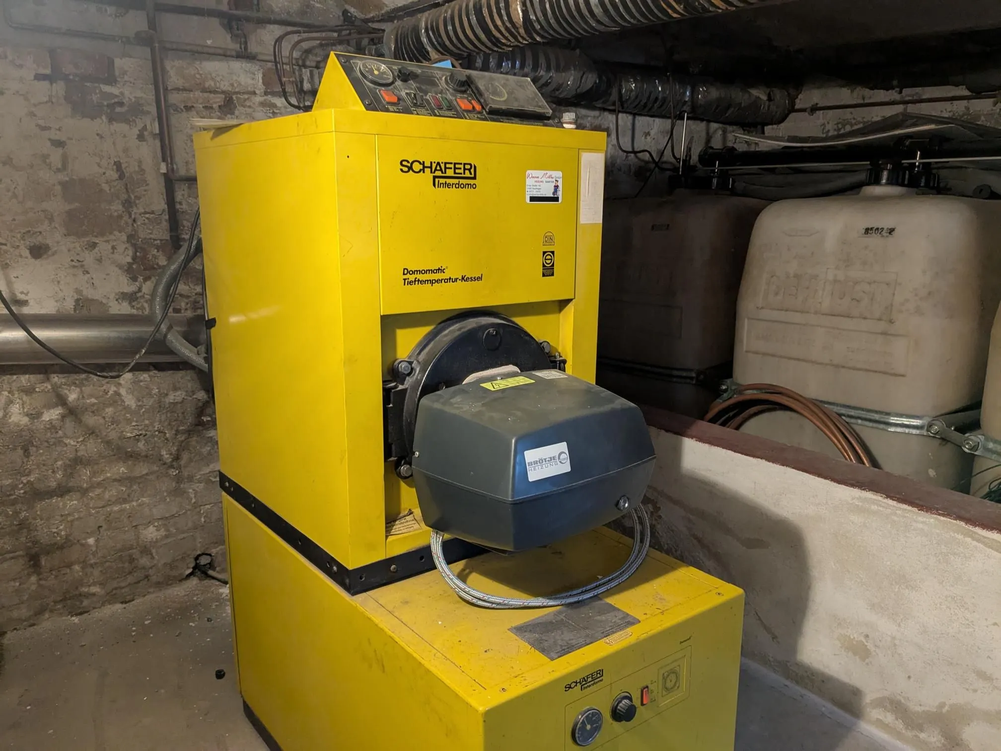 Eine alte, gelbe Ölheizung im Heizungskeller mit Kunststoff-Öltanks.