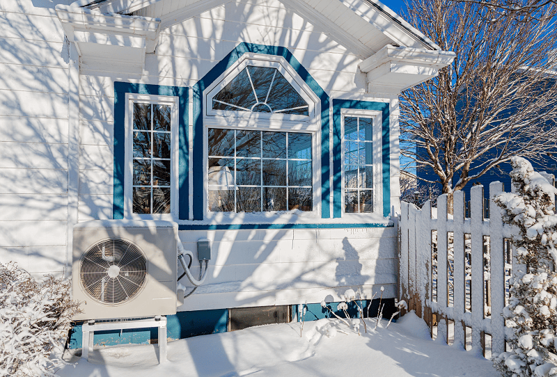 Luftwärmepumpe vor einem weißen Haus im Schnee.