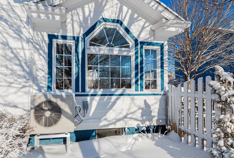 Luftwärmepumpe vor einem weißen Haus im Schnee.