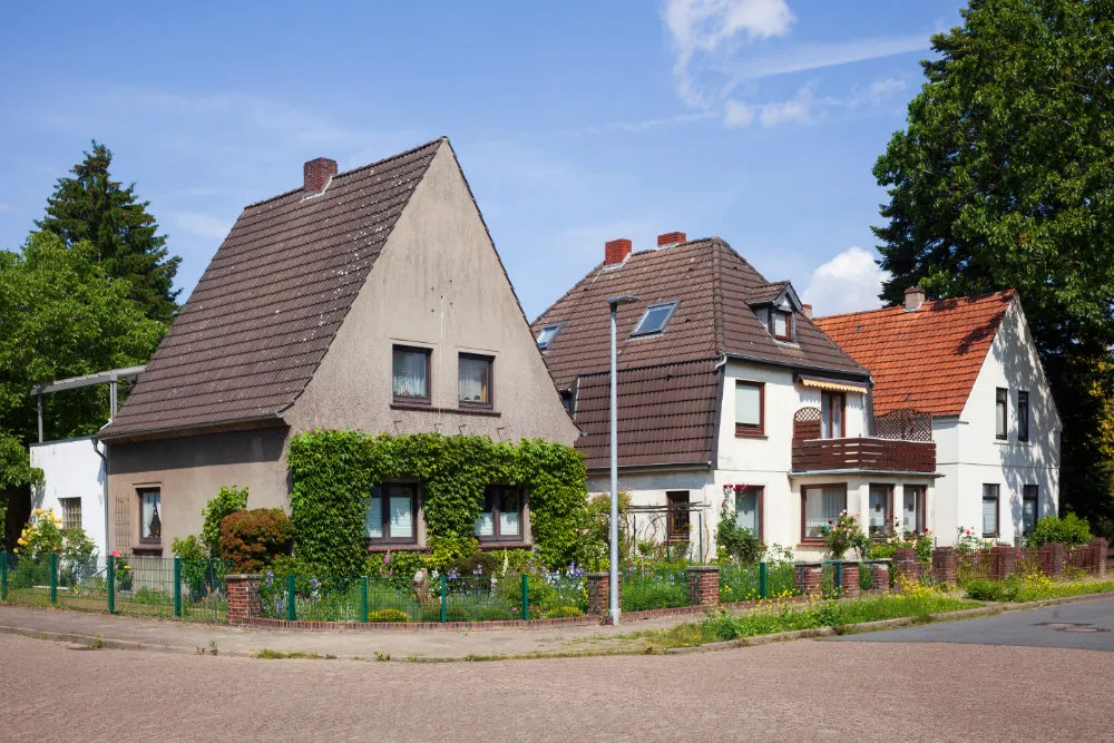 Reihen von Einfamilienhäusern mit Gärten an einer ruhigen Straßenecke unter blauem Himmel.