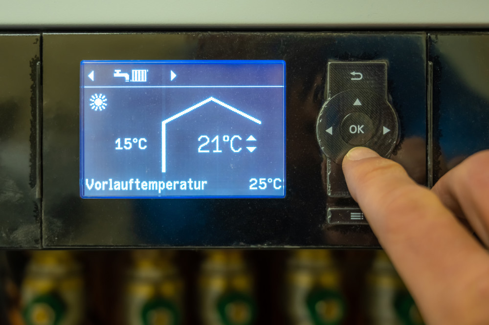 Hand stellt Vorlauftemperatur von 21 Grad Celsius an digitalem Heizungssteuergerät ein.