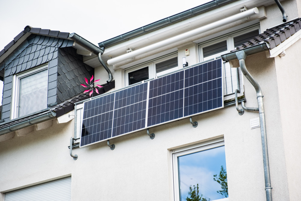 Balkon eines Hauses mit vier an der Brüstung montierten Solarpanelen.