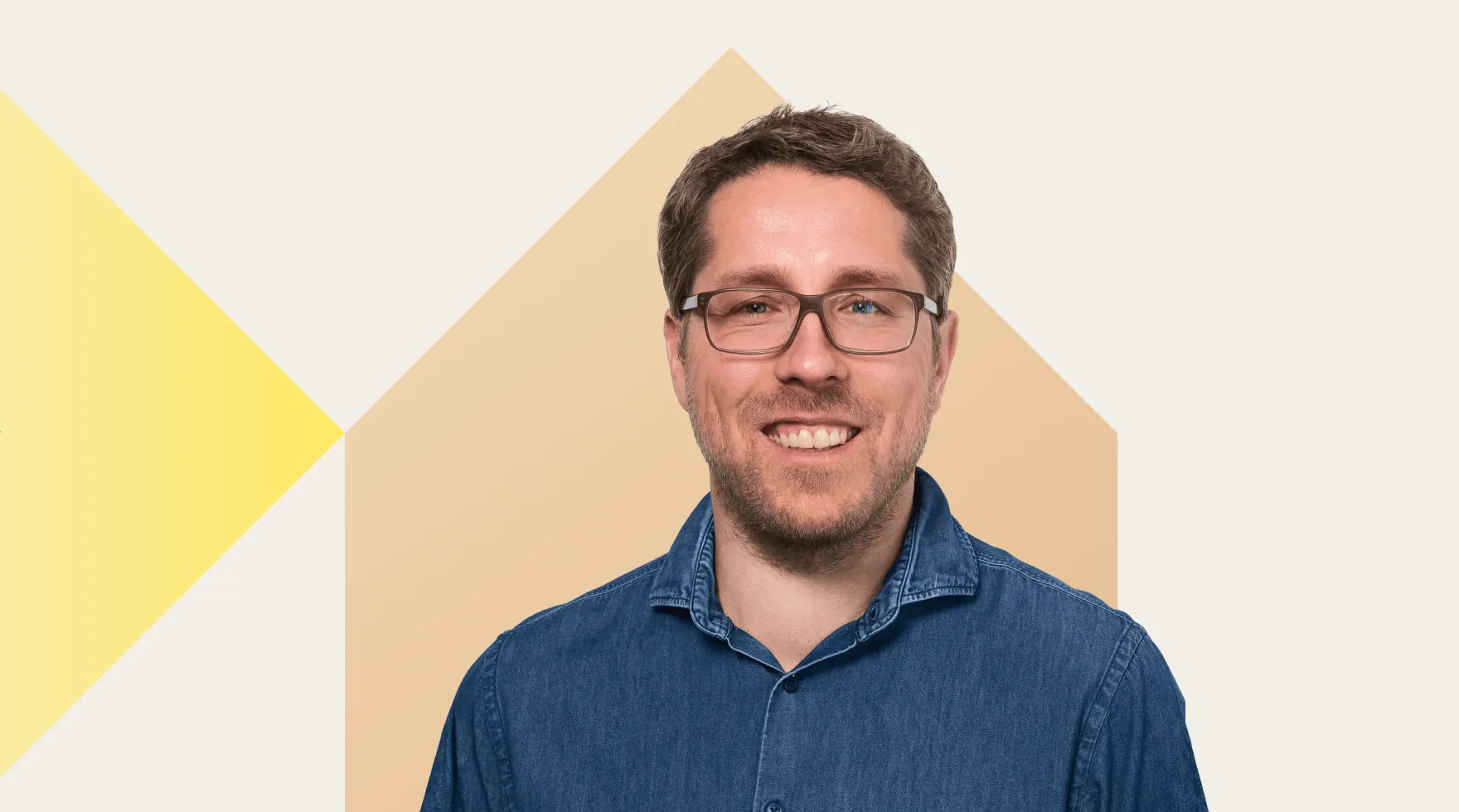 Mann mit Brille und Jeanshemd lächelt vor einem abstrakten Hintergrund mit gelbem und beigefarbenem Dreieck.