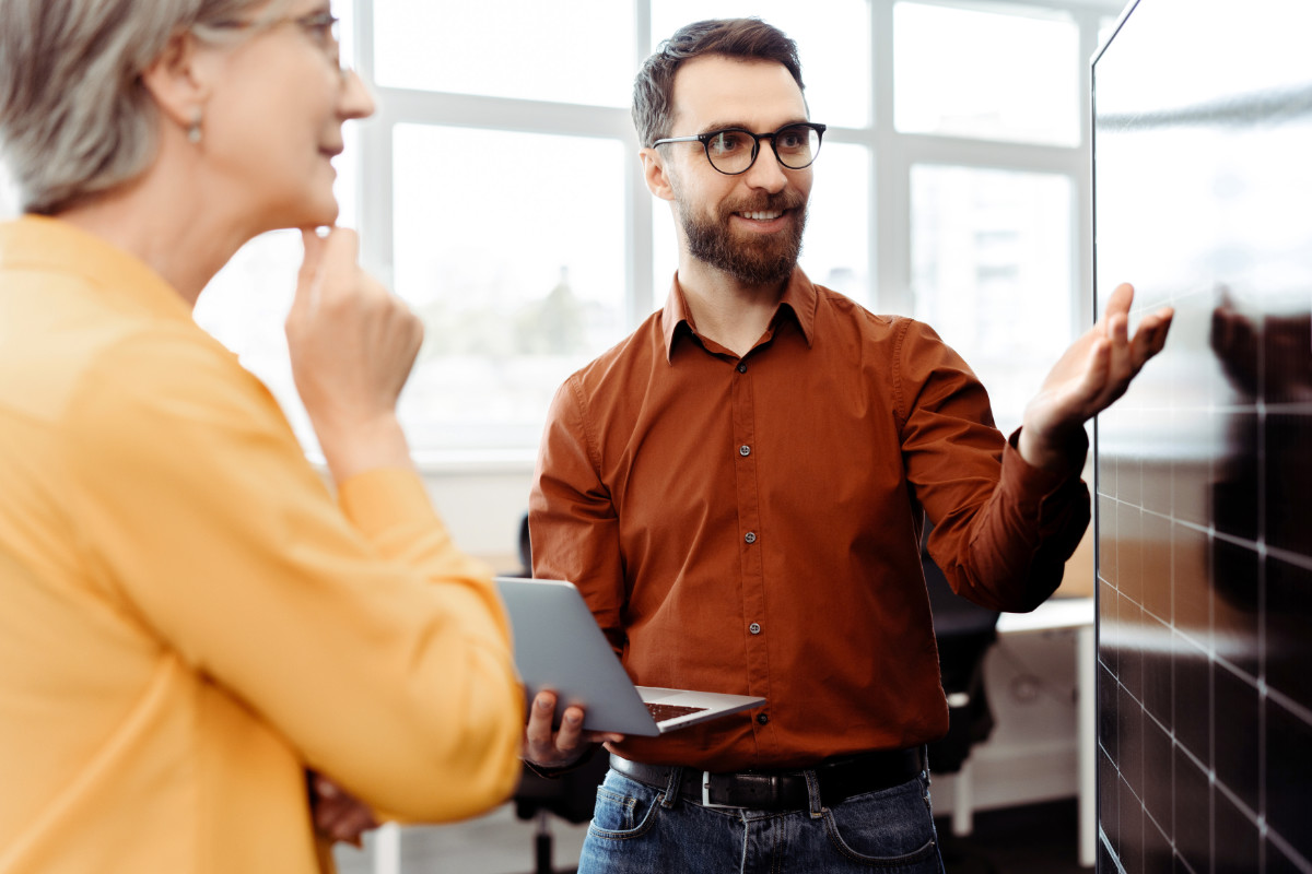 Ein Mann erklärt einer Frau ein schwarzes Solarpanel in einem hellen Büro.