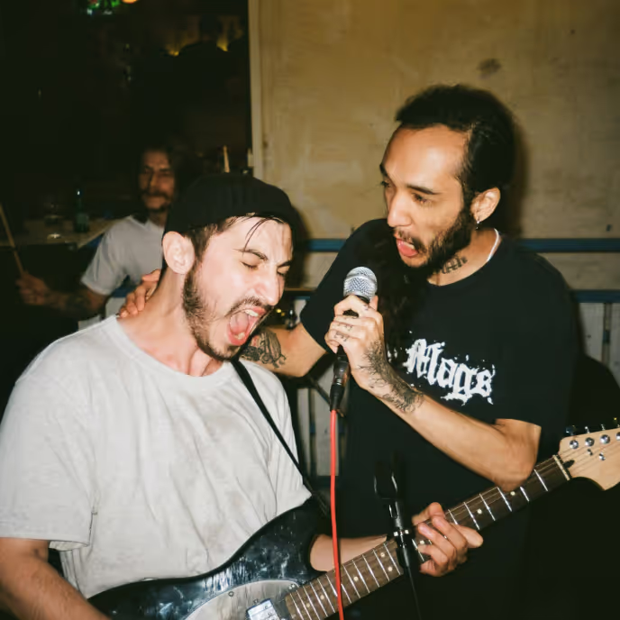 Two male artists performing, one holding a microphone and one playing guitar