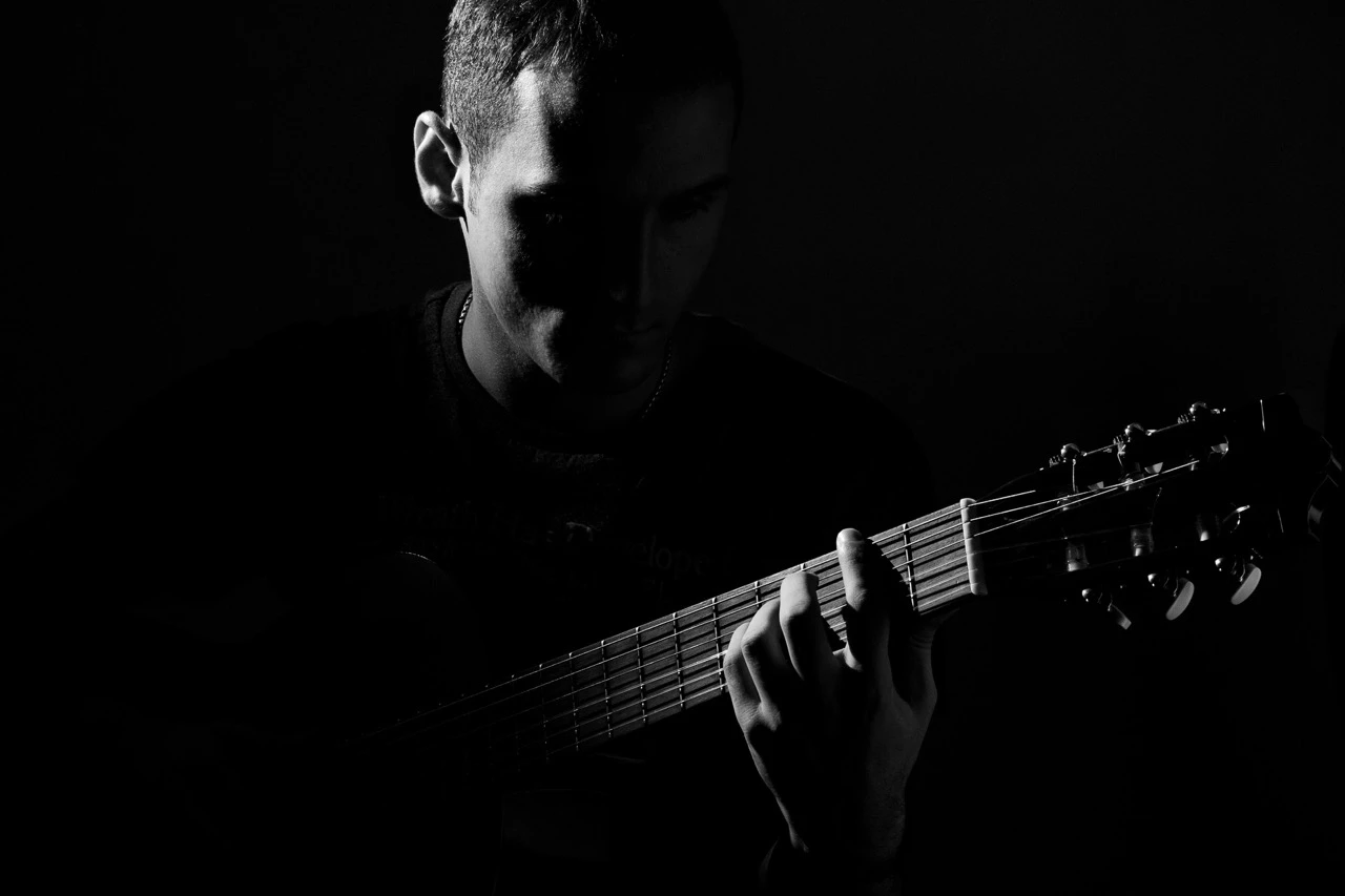 Black and white image of a male artist playing guitar in the shadows
