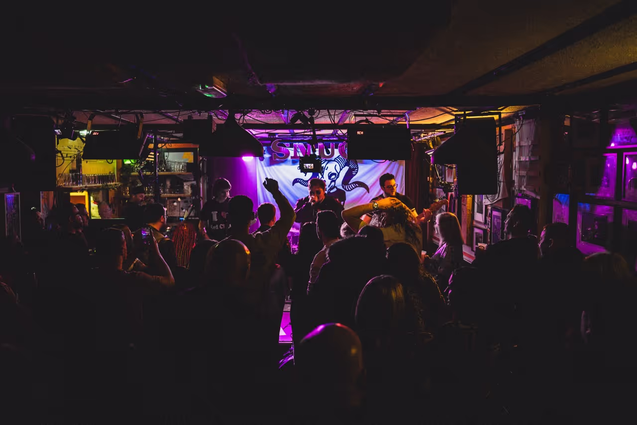 A crowd of people gathered in a dimly lit room illuminated by vibrant purple lights