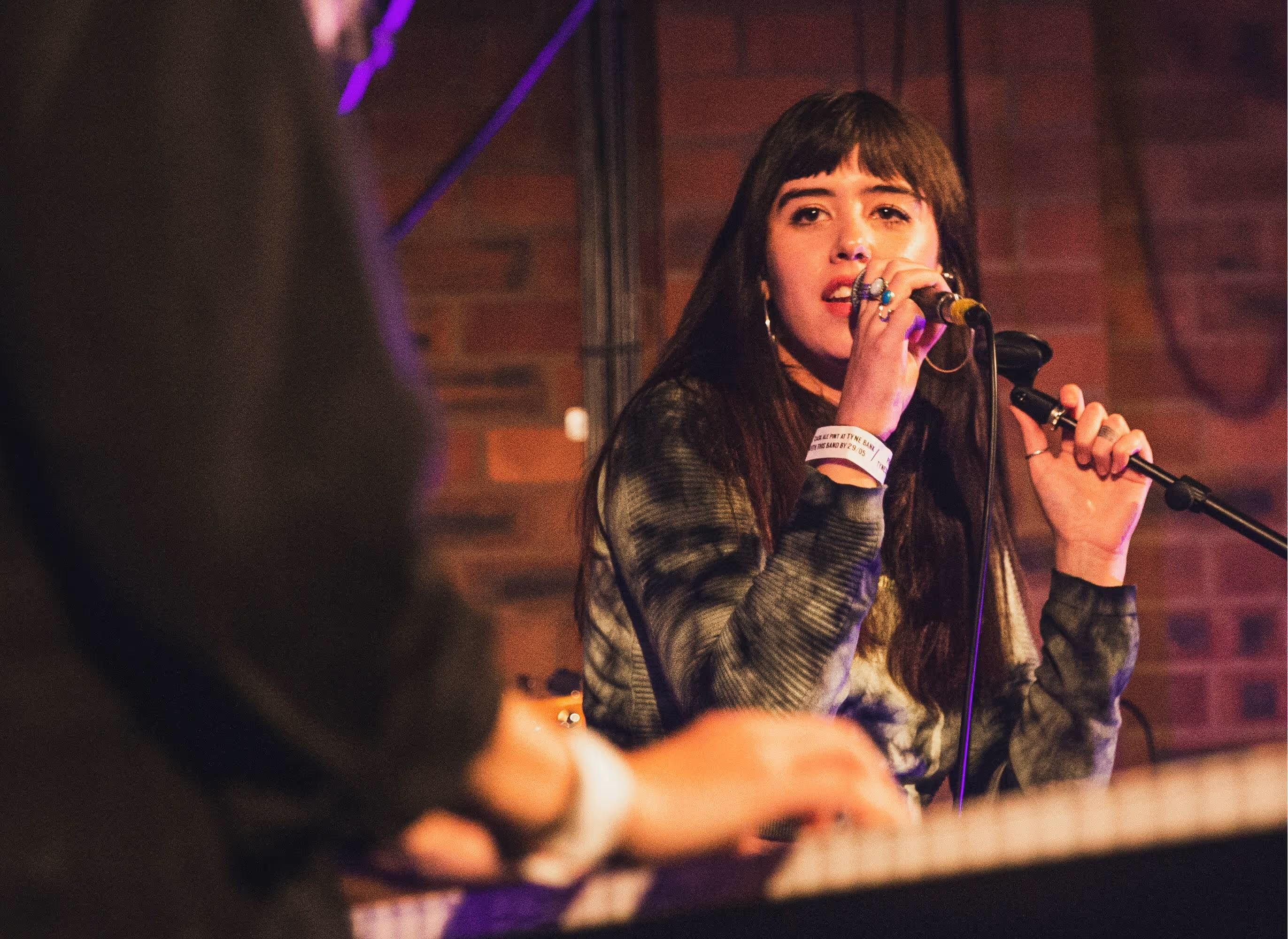 Female musicians on stage: one singing into a mic, the other playing the keyboard.
