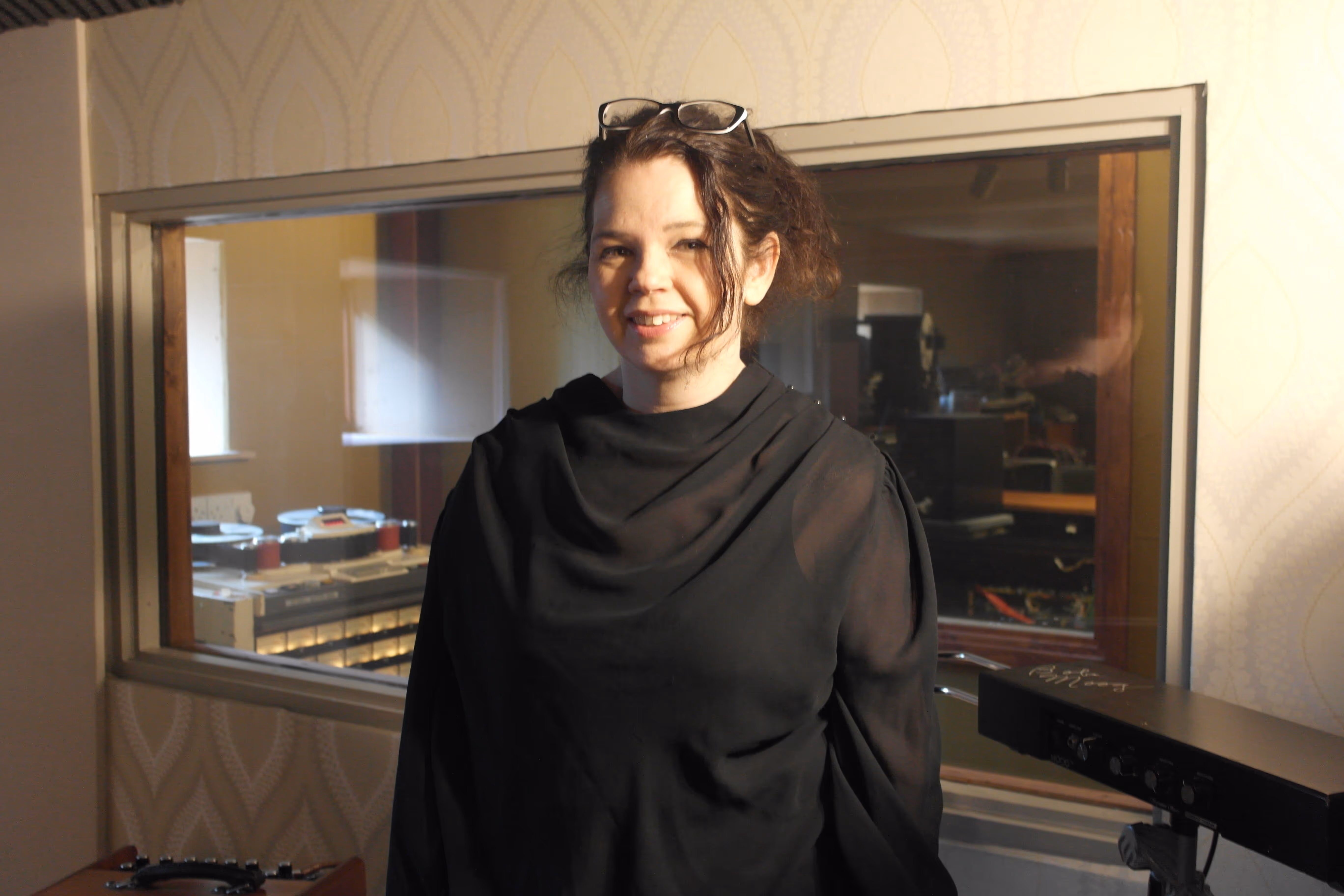 Image of a woman in black smiling at the camera in a music studio