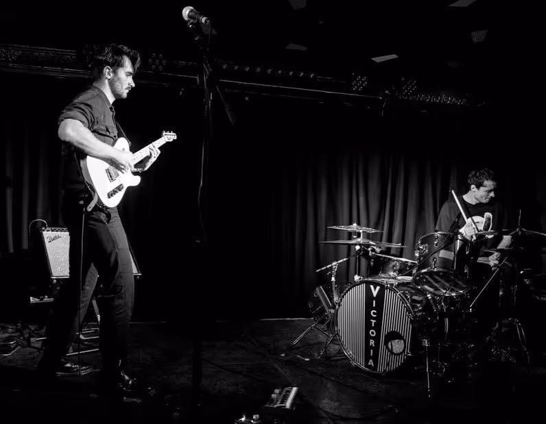 A black and white image of a guitarist and drummer playing music together 