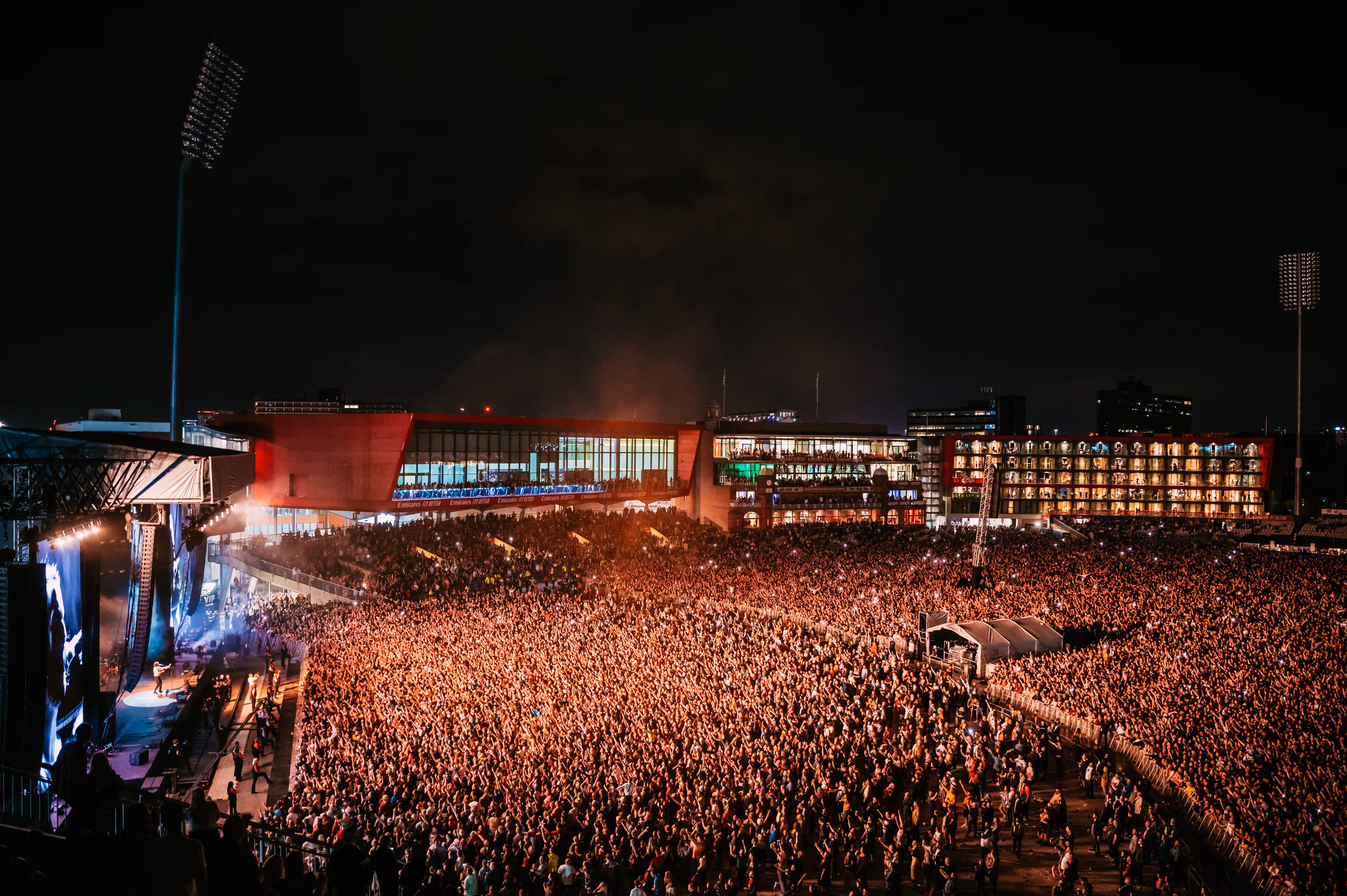 A vibrant crowd of concertgoers stands before a stadium, immersed in the excitement of a live performance.