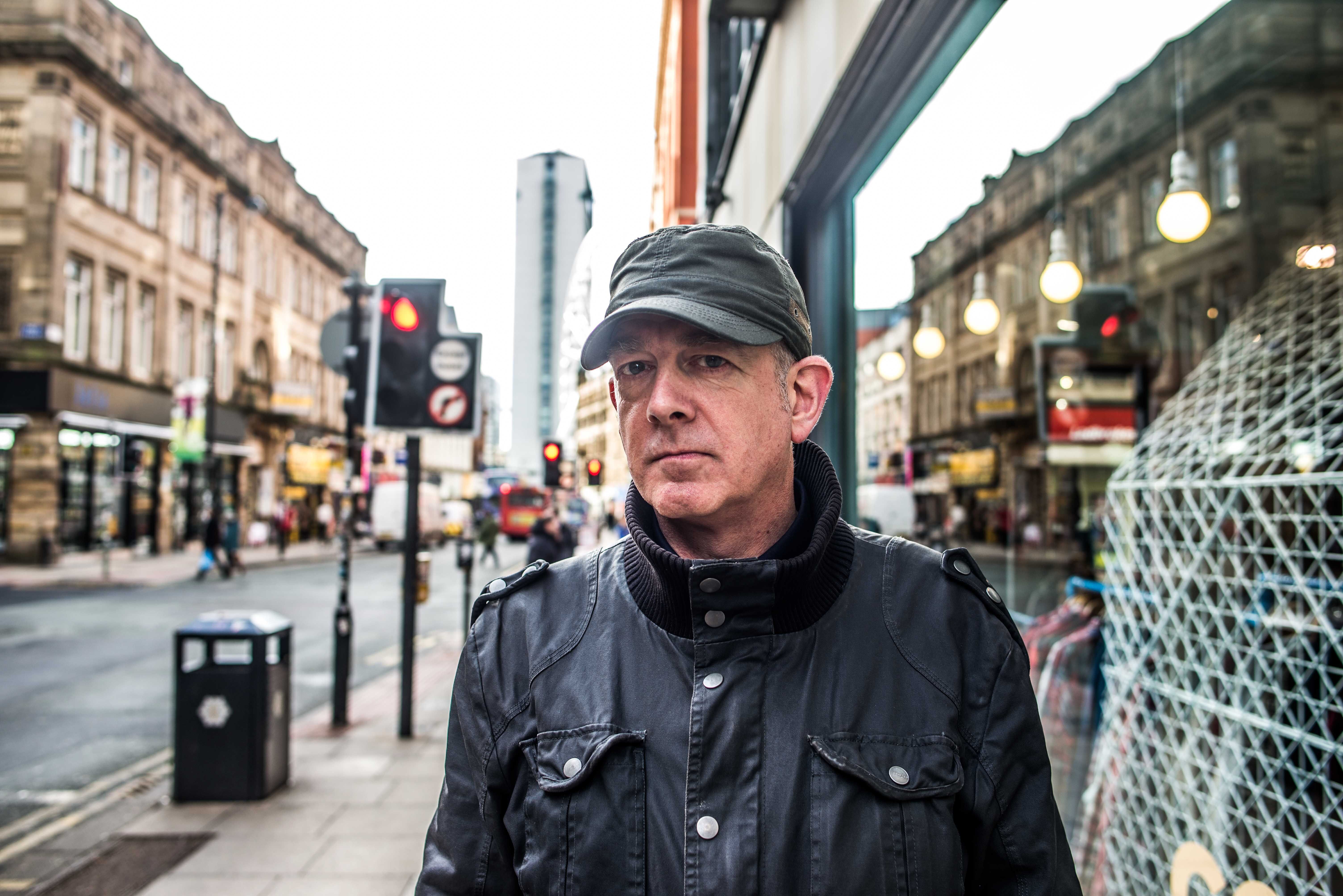 A shot of a man looking into the camera in a serious manner wearing a black jacket and khaki cap