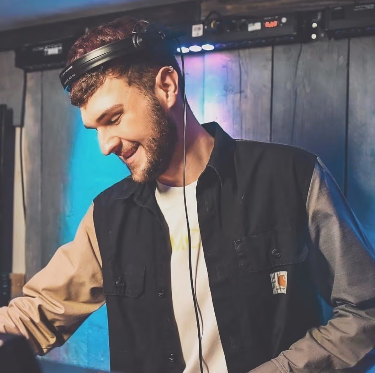 A man wearing headphones on his head smiles whilst looking down