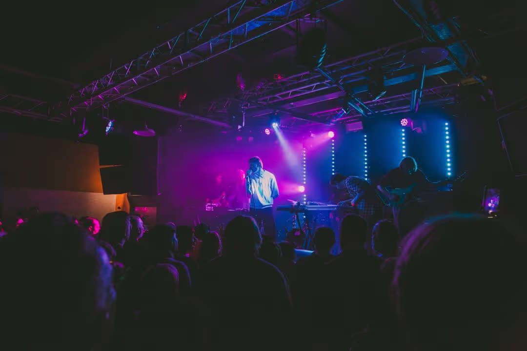 A vibrant crowd enjoying a concert illuminated by striking purple lights, creating an energetic atmosphere