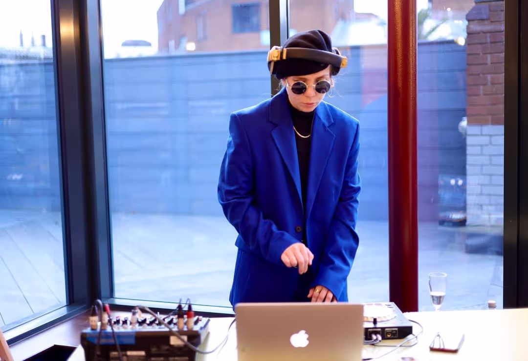 A blurry shot of a female DJ mixing tracks at a laptop and music station in a lively club