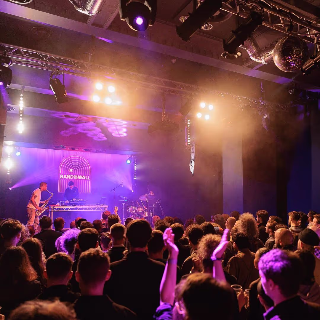 A vibrant crowd enjoying a concert illuminated by striking purple lights, creating an energetic atmosphere