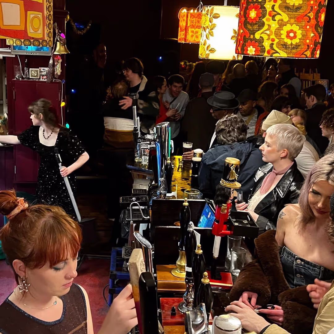 A woman is pulling a pint behind the bar, highlighting the lively setting and social environment of the establishment