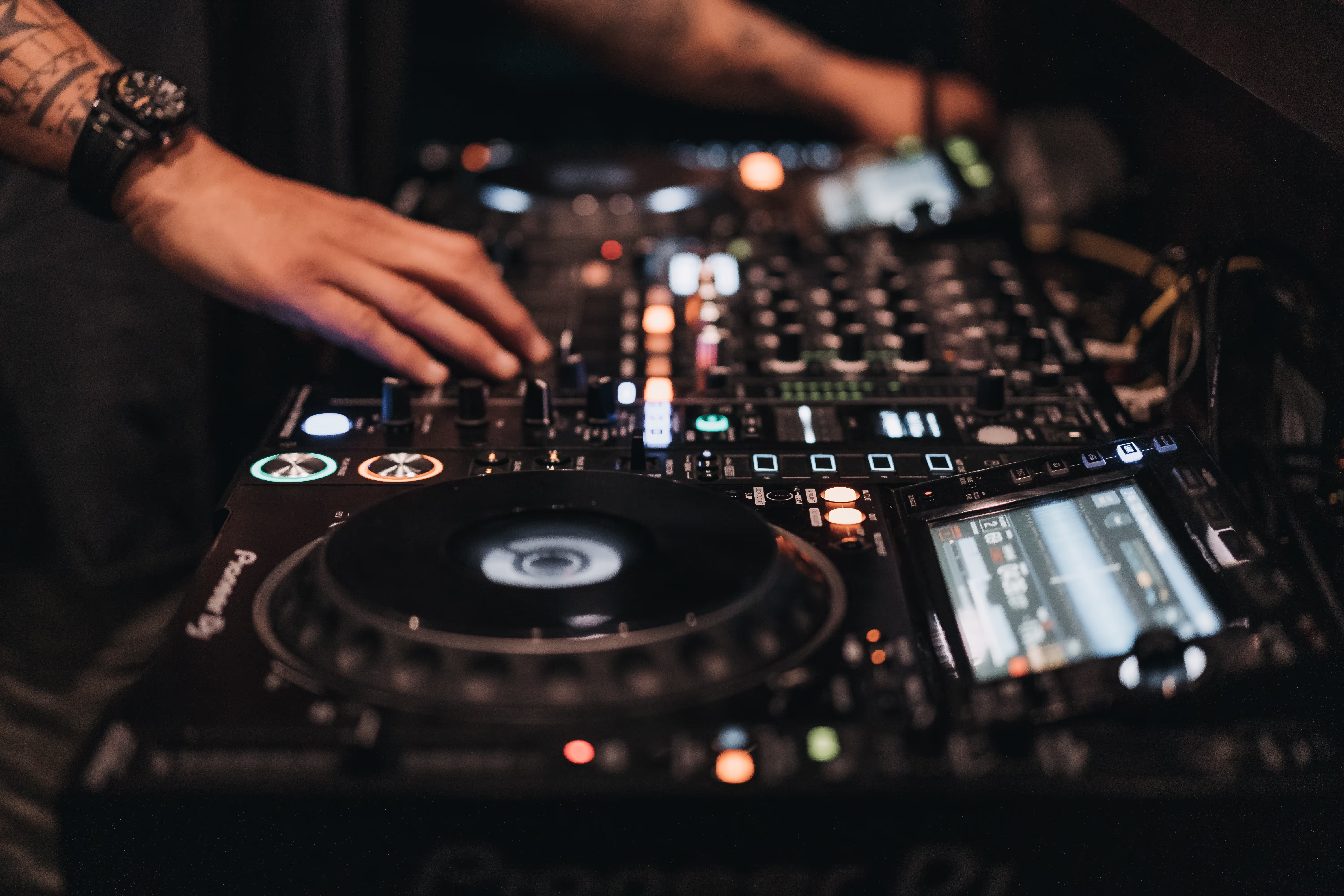 A DJ focused on mixing tracks using a DJ mixer, surrounded by vibrant lights and an engaged audience