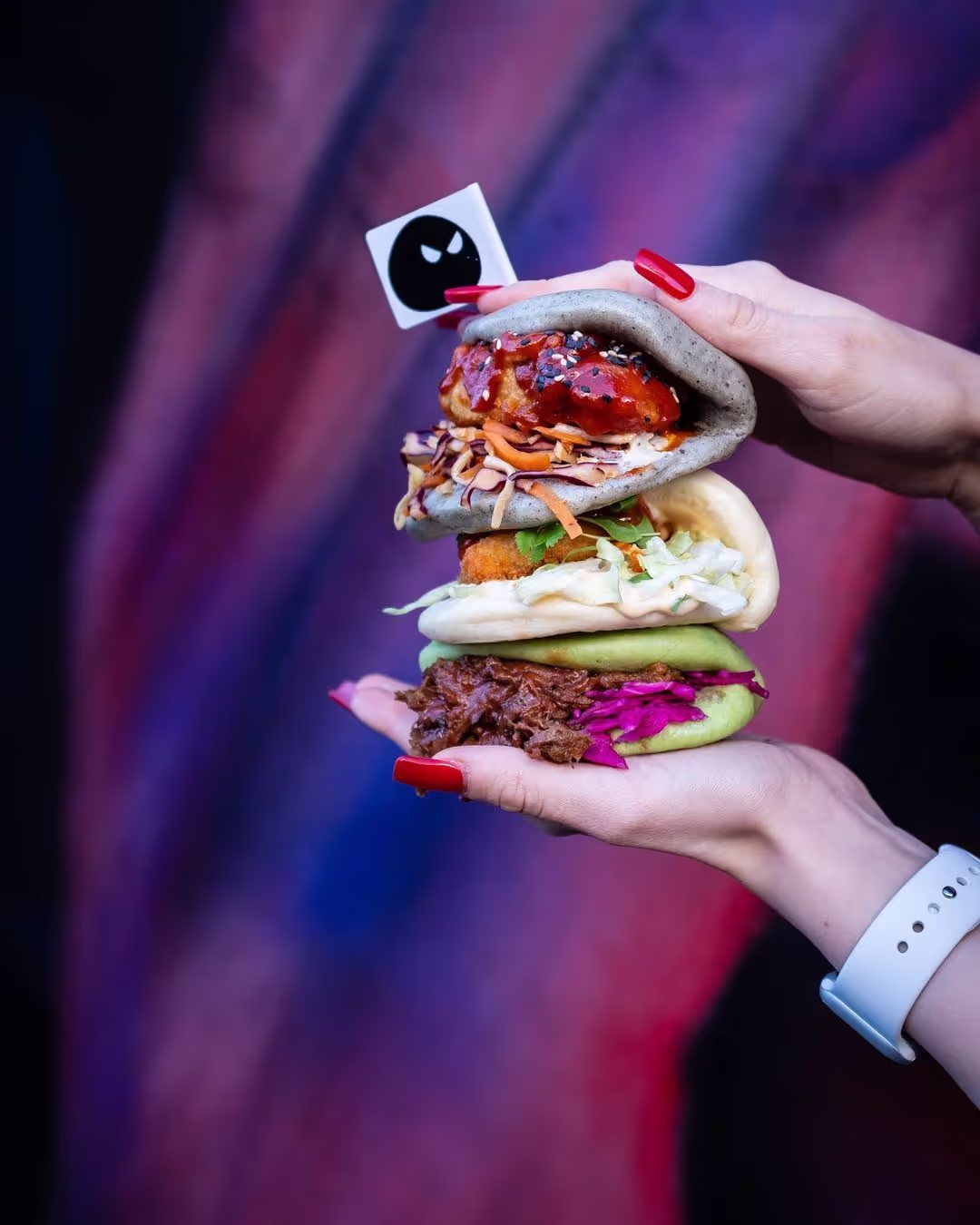 Two hands hold a pile of three tasty filled bao buns